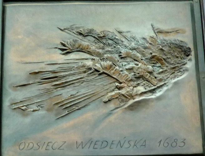 Płaskorzeźba. Przedstawia odsiecz wiedeńską i pędzących żołnierzy. Pod sceną napis: Odsiecz wiedeńska 1683.  Jest to dekoracja drzwi z łacińską inskrypcją "Milito pro Christo" i przedstawia 8 bitew, w których Polacy walczyli w obronie kraju.