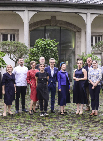 Grupa ludzi pozuje do zdjęcia przed budynkiem z kolumienkami.